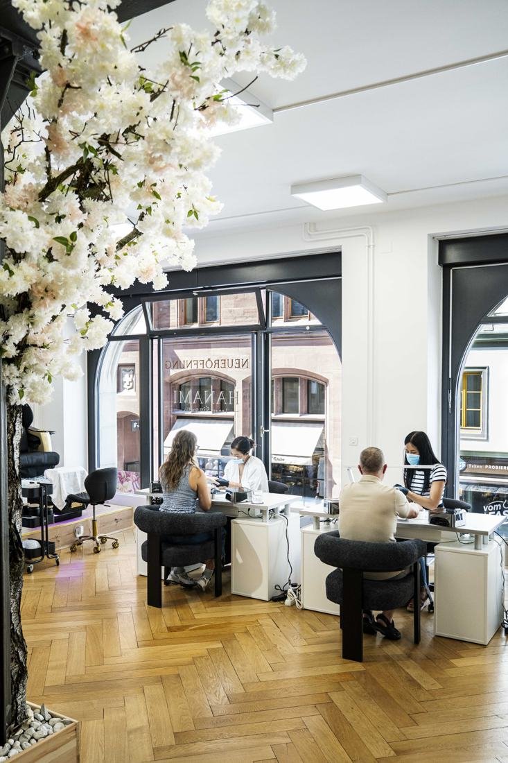 Blick in den hellen Salon mit Kirschblütenzweigen, Fischgrätparkett und Maniküre-Tischen